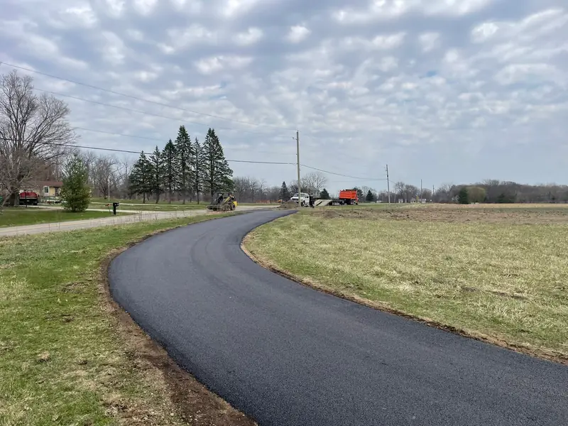New asphalt driveway sweeping in a long curve between a lawn and an open field