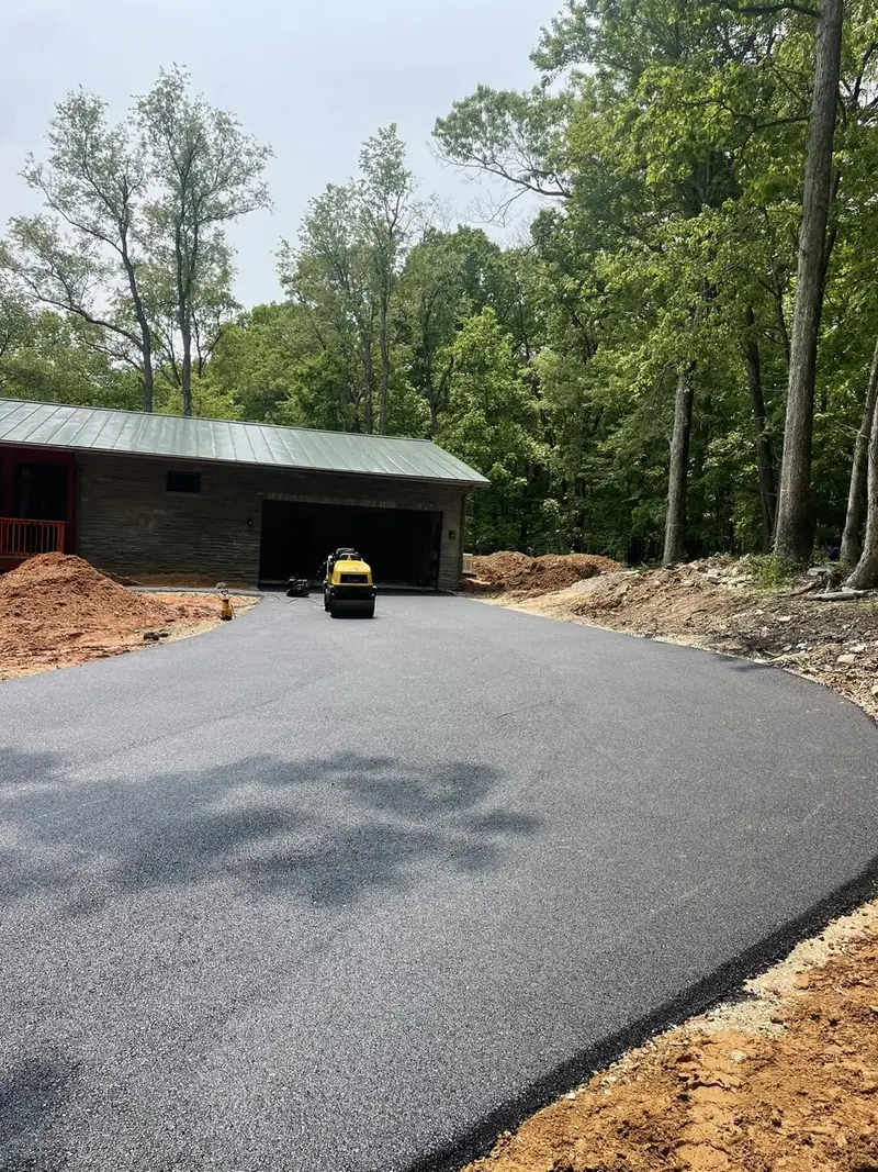 New asphalt driveway and turnaround in front of a garage, with the roller still on site