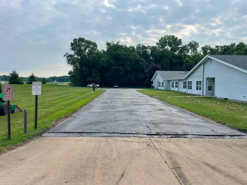 Before: a cracked, patched asphalt entrance drive and parking row