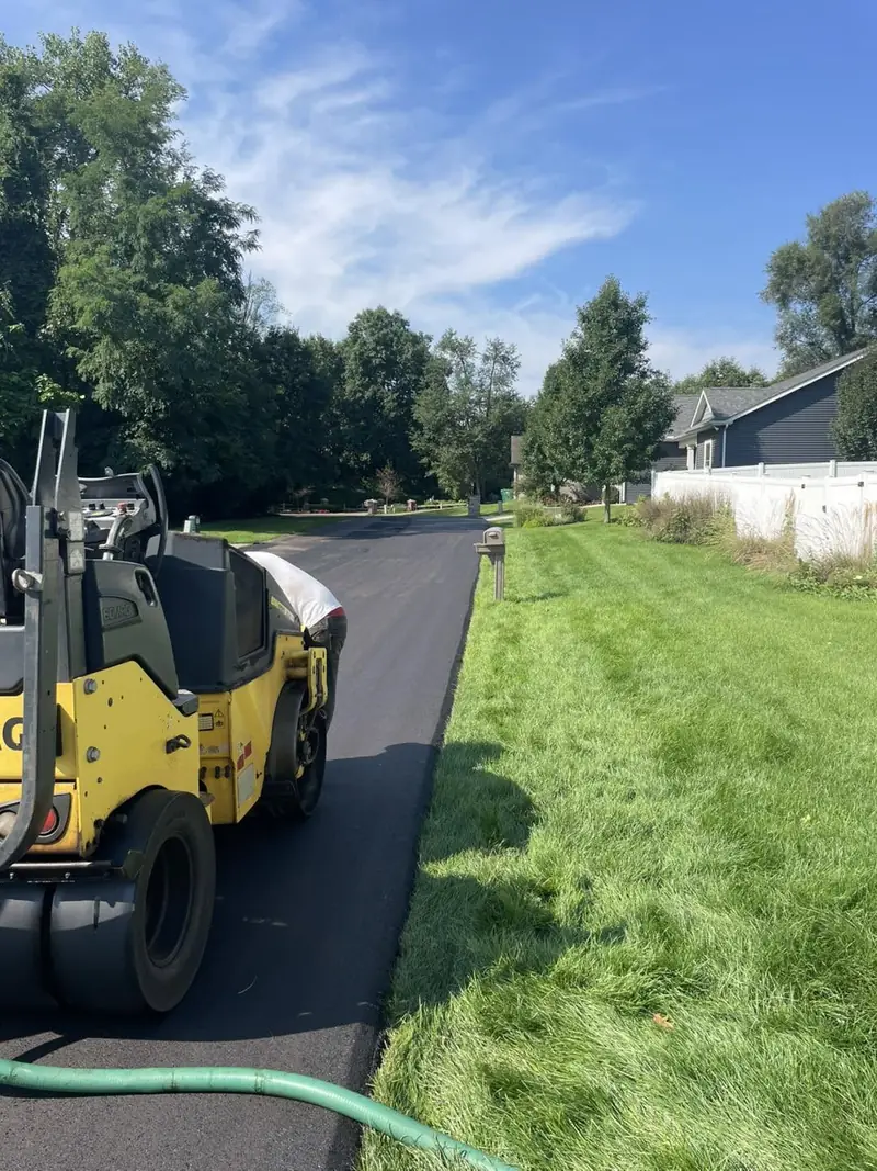 Roller compacting a narrow new driveway along a freshly mowed lawn