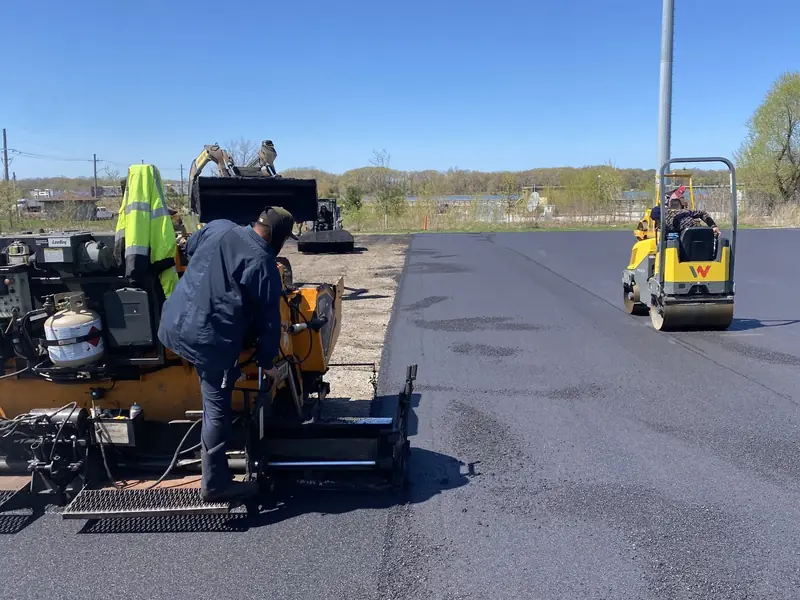 Asphalt paver and tandem roller working a new parking lot under a clear sky