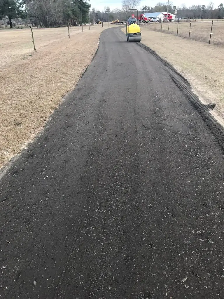 Ride-on roller compacting a long rural asphalt lane between fence lines